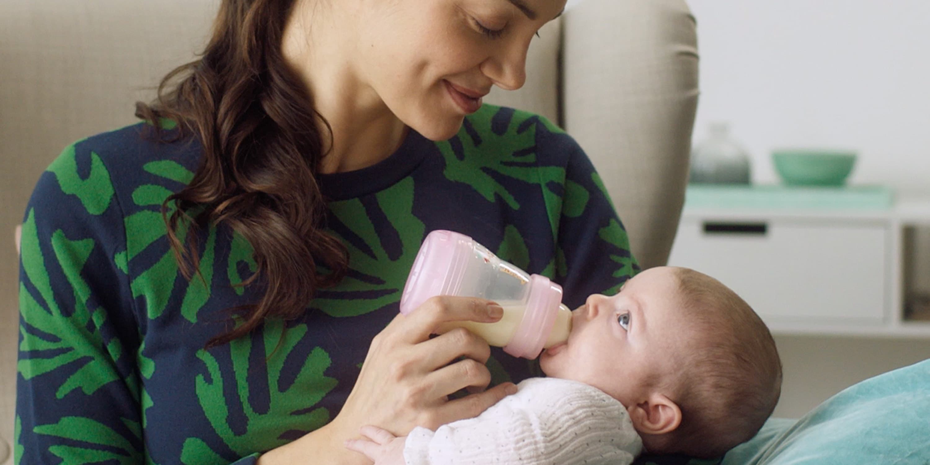 Mother feeds her little daughter with the baby bottle, close-up